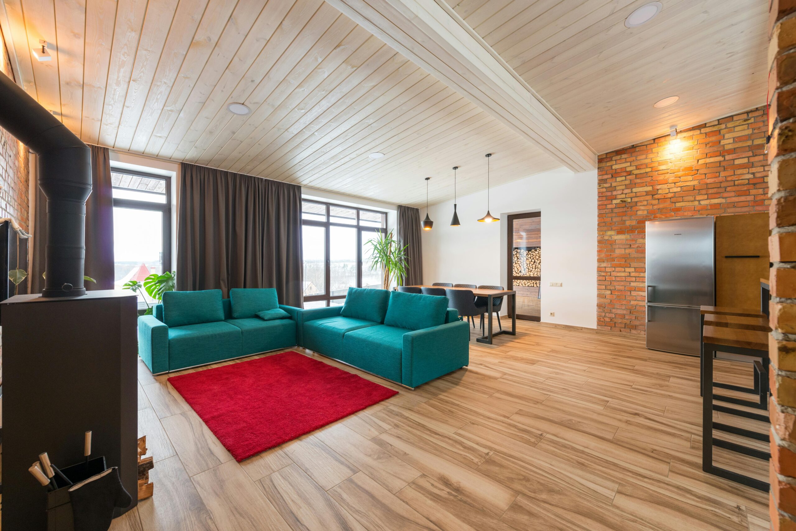 Spacious and stylish living room featuring a teal sofa, brick wall, and modern design elements.